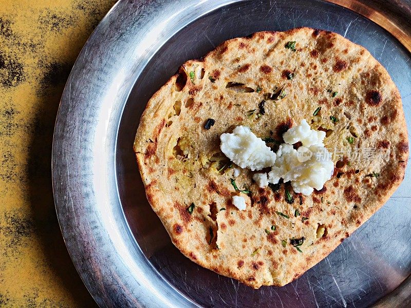 Amritsari Aloo-Paratha的水平点击，库尔查塞满了土豆，洋葱，绿色丹尼亚和香料与白黄油makkhan在一个钢板或塔利放在一个木制表面。
